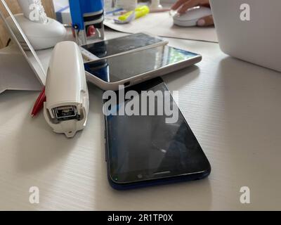 Two working touchscreen mobile phones, smartphones lie on the table in the office with stationery, a stapler, a seal and a laptop. Stock Photo