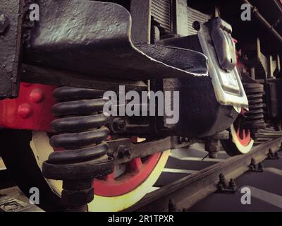 Large iron wheels of a red and black train standing on rails and suspension elements with springs of an old industrial steam locomotive. Stock Photo