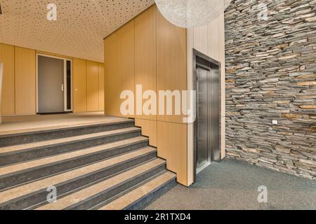 some stairs in a building with stone walls and wood panels on the wall behind it is a staircase leading up to an elevator Stock Photo