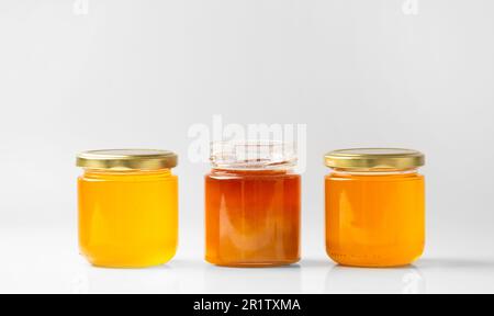 Conceptual composition of open and closed jars with different honey on isolation. Multi-colored honey in jars on a white background close-up. Stock Photo