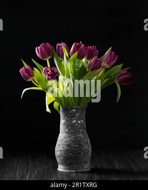 Purple tulips in a handmade vase on a dark background. Lots of beautiful purple tulips on a black background. Spring flowers in a vase. Stock Photo