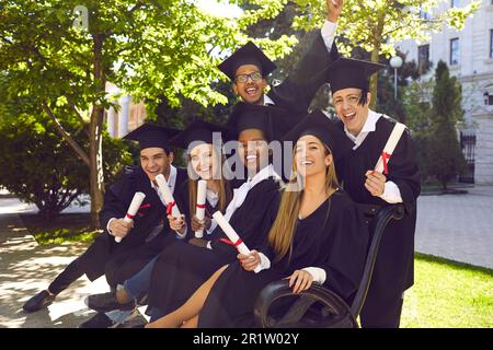 Portrait of multinational group of students in mortar boards cap and ceremonial robes holding diploma in their hands. Stock Photo