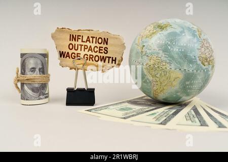 Business and finance concept. On the table are dollars, a globe and there is a sign with the inscription - inflation outpaces wage growth Stock Photo