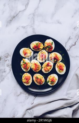 Stuffed deviled eggs with salmon and mayonnaise. Easter food concept, spring flowers, easter bunny. Homemade deviled eggs with salmon on a black backg Stock Photo