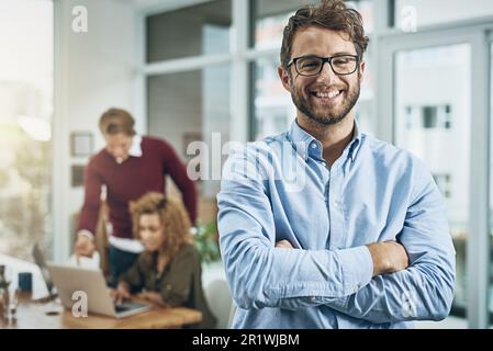Superb managerial skills that make an impact on business. Portrait of a confident young man with his colleagues in the background at work. Stock Photo