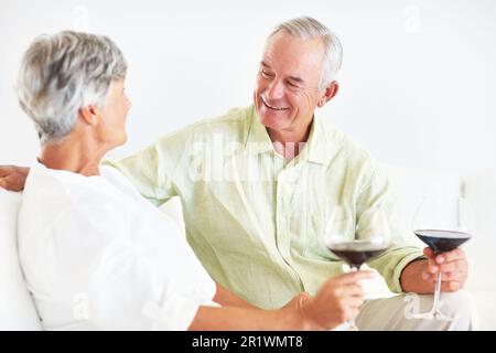 Mature couple drinking wine on couch. Happy mature man and woman drinking wine while sitting on couch. Stock Photo