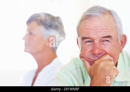 Mature couple after fight. Closeup of pensive mature man looking away with upset woman in background. Stock Photo