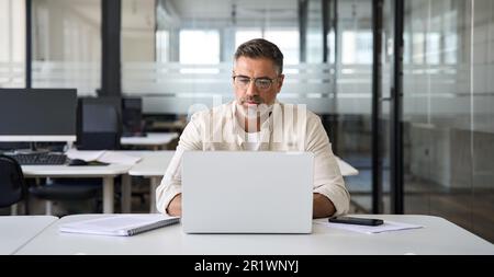 Mature Latin business man ceo trader using computer working in modern office Stock Photo