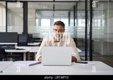 Mature Latin business man ceo trader using computer working in modern office Stock Photo