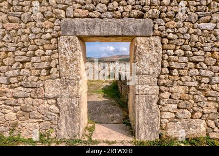 Looking through a doorway in a restored stone wall in the ancient former Roman city of Volubilis in northern Morocco, with a view of more ruins and th Stock Photo