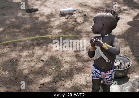 Omo Valley, Ethiopa â€“ 11.17.2022: young Mursi boy looks for his mother in a tribal village Stock Photo