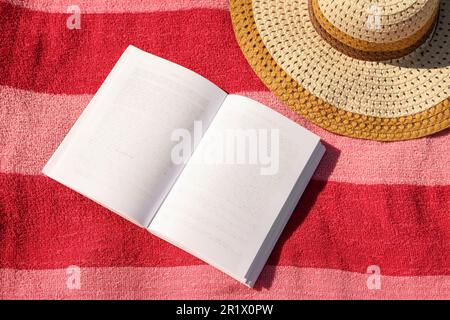 Open book and hat on striped beach towel, top view Stock Photo