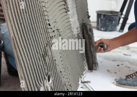 Worker spreading adhesive mix over tile with spatula, closeup Stock Photo