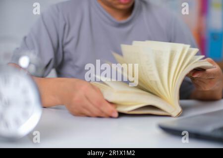 Closeup image of Asian woman sitting at a table reading a book in the living room. Stock Photo