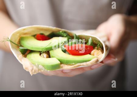 Woman holding delicious hummus wrap with vegetables, closeup Stock Photo