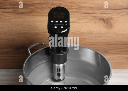 Sous vide cooker in pot on white wooden table. Thermal immersion circulator Stock Photo
