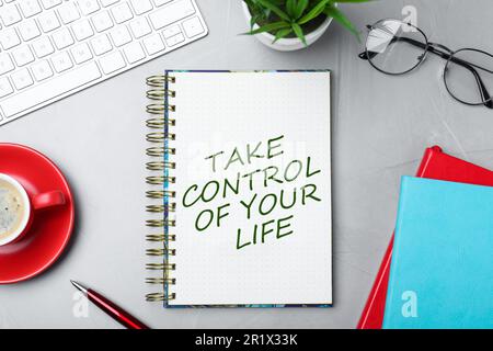 Phrase Take Control of Your Life in notebook, office stationery and cup of coffee on light grey table, flat lay Stock Photo