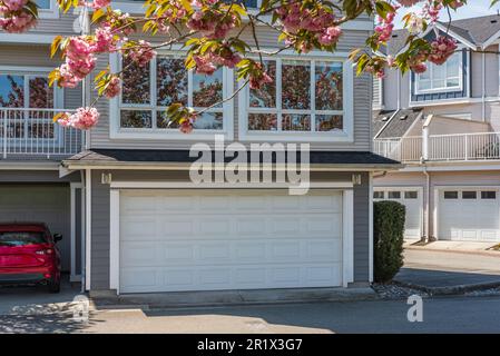 Garage door with short driveway. Nice neighborhood on a sunny day. Row of garage doors at parking area for townhouses. Exterior of house with concrete Stock Photo