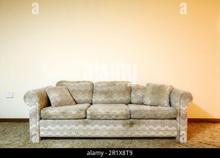 A dirty couch sitting in front of a starkly empty wall.  This house has since been demolished. Stock Photo