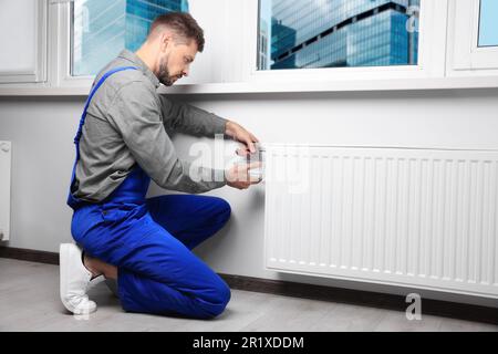 Professional plumber using pliers while preparing heating radiator for winter season in room Stock Photo