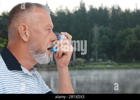 Mature man using asthma inhaler near forest. Emergency first aid during outdoor recreation Stock Photo