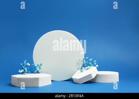 Product photography props. Podiums of different geometric shapes and flowers on blue background Stock Photo