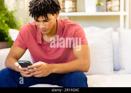 Smiling biracial man using smartphone sitting on sofa in living room Stock Photo