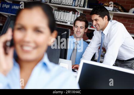 Satisfied with the result. Two colleagues collaborating on a project together while a businesswoman takes a call in the foreground. Stock Photo
