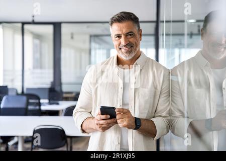 Middle aged hispanic employee standing with phone and looking at camera. Stock Photo