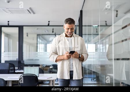 Smiling mature businessman holding and using smartphone applications in office.  Stock Photo
