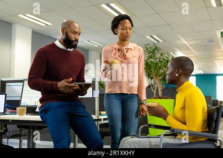 African american businesswoman sitting on wheelchair and discussing with colleagues in office Stock Photo
