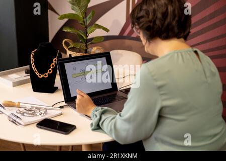 Caucasian female jeweller drawing sketches using laptop and graphics tablet at jewellery shop Stock Photo