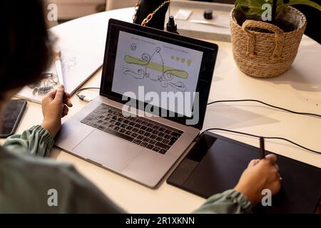Caucasian female jeweller drawing sketches using laptop and graphics tablet at jewellery shop Stock Photo