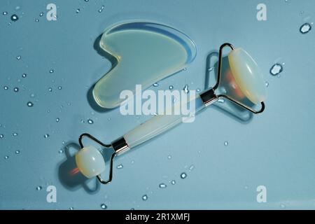 Blue jade face roller and Gua Sha scraping for beauty facial massage therapy on blue background with drops of water. Concept of freshness and cleanlin Stock Photo