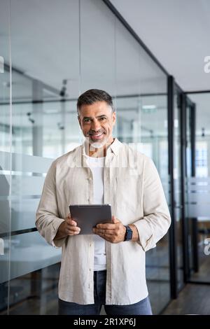 Vertical portrait of Indian senior businessman CEO using apps on digital tablet. Stock Photo