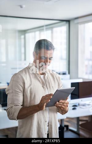 Vertical portrait Latin mature adult professional business man using tablet. Stock Photo