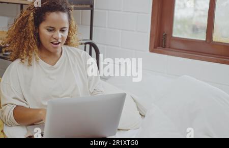 Young woman using laptop on bed at home in the morning. Stock Photo