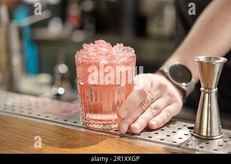 Bartender holding fresh delicious red summer cocktail in glass decorated with ice Stock Photo