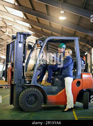 Getting pallets where they need to go. driver in a forklift and a manager on the factory floor. Stock Photo