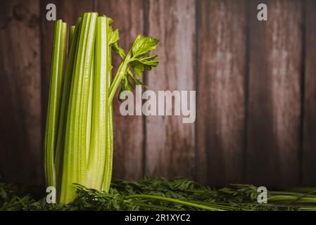 Still life of a celery plant on green leaves and wooden background. Stock Photo