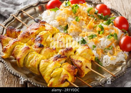 Grilled saffron chicken skewers with rice garnish close-up in a plate on a wooden table. horizontal Stock Photo