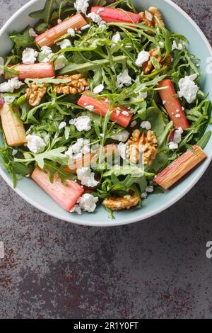 Rhubarb salad with arugula, goat cheese and walnuts close-up in a bowl on the table. Vertical top view from above Stock Photo
