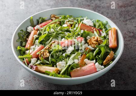 Diet salad with baked rhubarb, arugula, goat cheese and walnuts close-up in a bowl on the table. Horizontal Stock Photo
