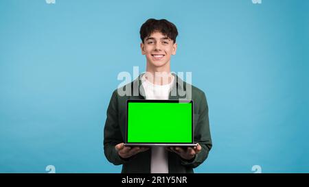 Young man smiling and showing laptop with green screen into the camera on a blue background Stock Photo