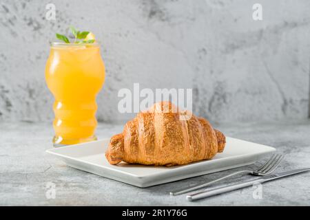 Croissant on a white porcelain plate with freshly squeezed orange juice on the side Stock Photo