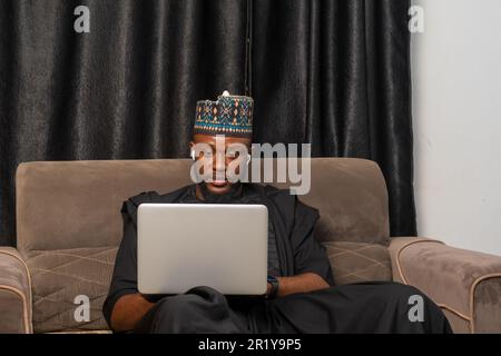 Good looking businessman in Africa attire seated working on his laptop to perform business transactions Stock Photo