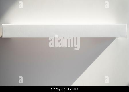 Long thin cardboard white box on paper surface with shadows and sunlight as mockup, top view, space for text Stock Photo