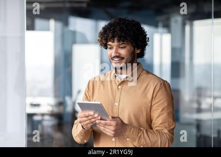 A smiling young Muslim man, businessman, student, designer standing in the office and using a tablet Stock Photo