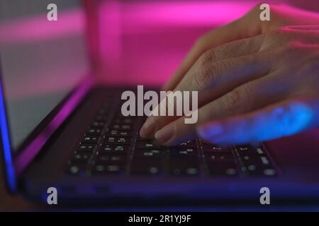Person typing at laptop computer at night. Female uses keyboard, shakes buttons with fingers. Internet security, cyber attack. Trendy neon light. Crea Stock Photo