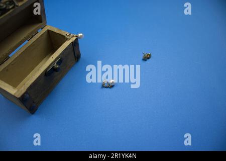 Open wooden chest with pearl earrings around it, placed on the edge of the blue background. Stock Photo